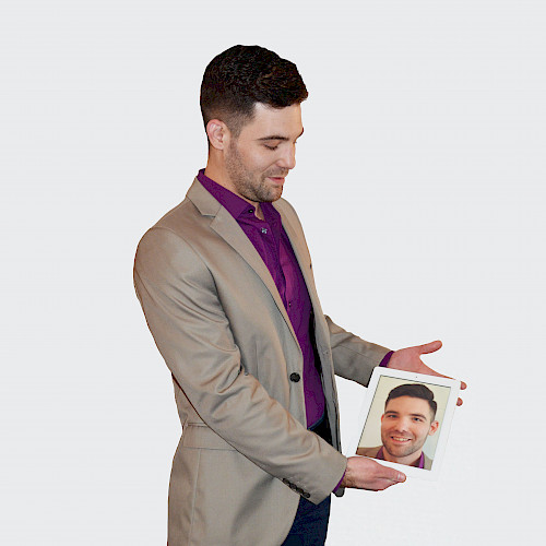 Porträt von M. Wigger, arbeitet in dem Steuerbüro Clemens, steht lächelnd im Anzug mit eine Bild von sich in der Hand.